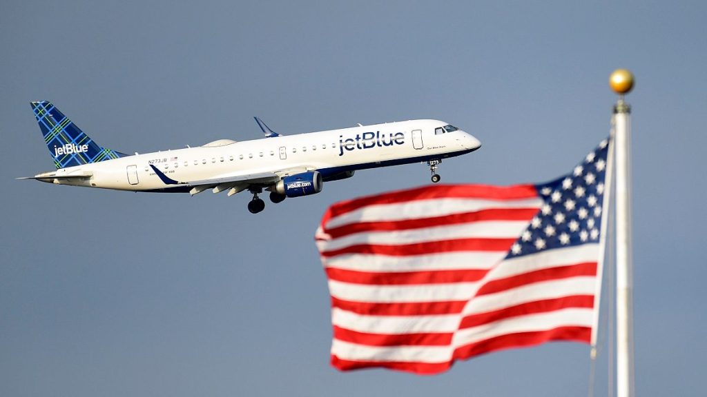 A JetBlue passenger jet flies past the US flag.