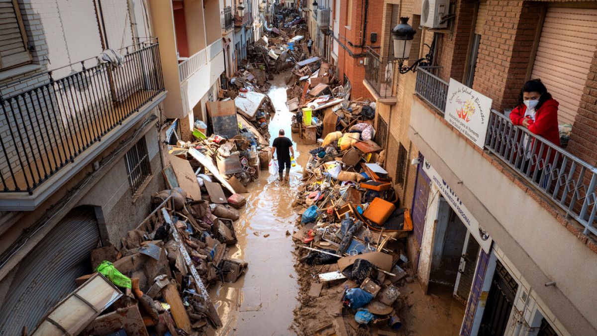 People walk through a street with piled furniture and rubbish on the sides in an area, affected by floods, in Paiporta, Valencia, Spain, Tuesday, Nov. 5, 2024.