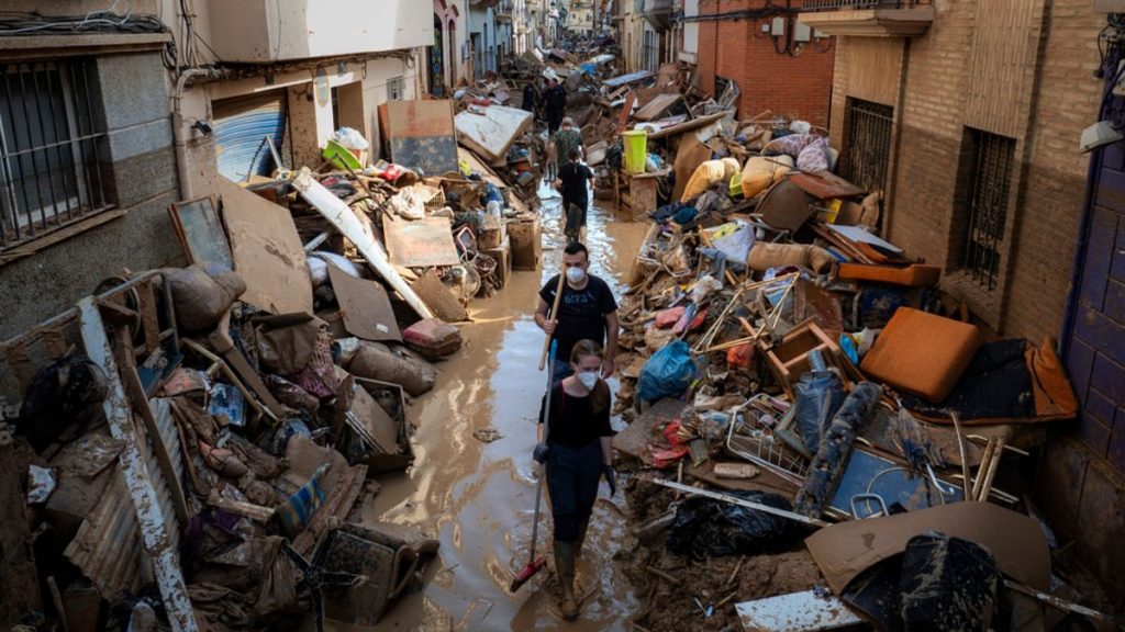 People walk through a street with piled furniture and rubbish on the sides in an area, affected by floods, in Paiporta, Valencia, Spain.