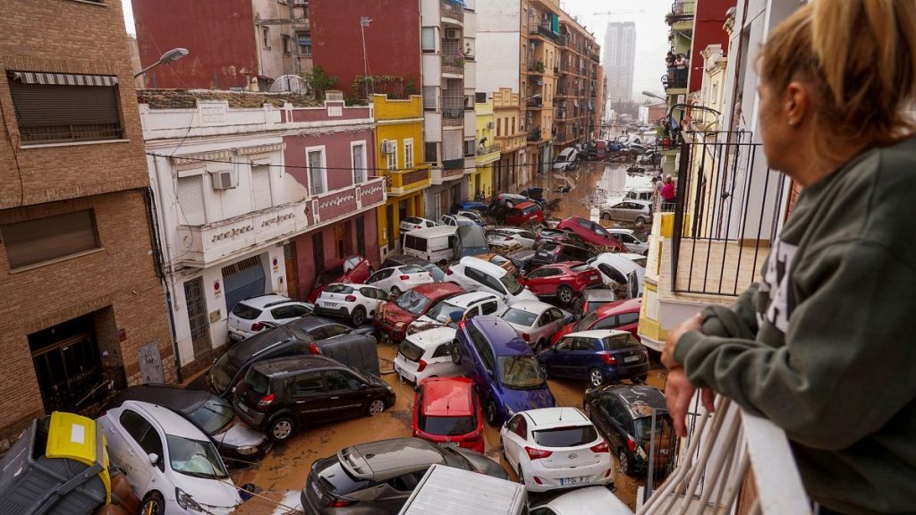 A woman looks out from her balcony as vehicles are trapped in the street during flooding in Valencia.