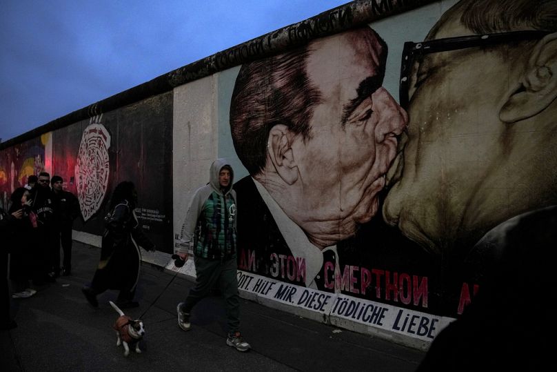 Des gens passent devant la soi-disant East Side Gallery, un lieu populaire pour le street art sur les vestiges du mur de Berlin, à Berlin, en Allemagne, le vendredi 8 novembre 2024. (Photo AP)