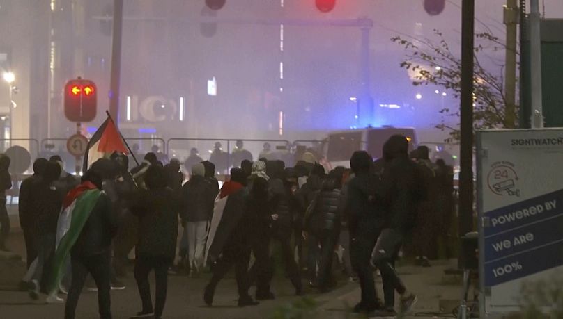 Un groupe de manifestants pro-palestiniens se dirige vers un cordon de police avec des fourgons de police circulant en arrière-plan à Amsterdam, le 7 novembre 2024.