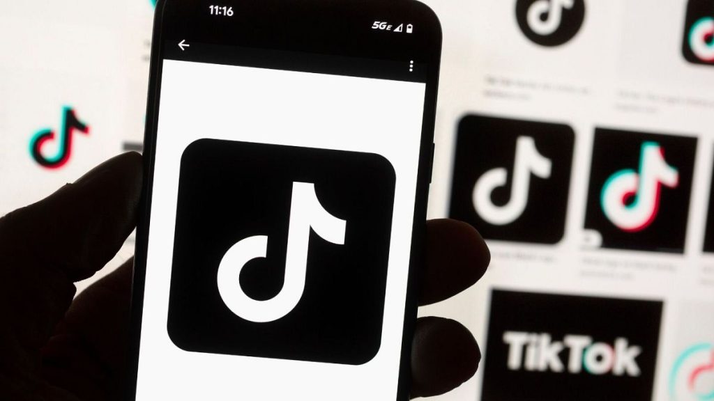 The TikTok logo is displayed on a mobile phone in front of a computer screen