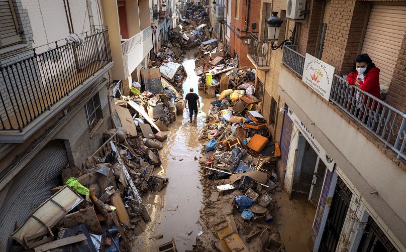 Les gens marchent dans une rue avec des meubles empilés et des déchets sur les côtés dans une zone touchée par les inondations, à Paiporta, Valence.