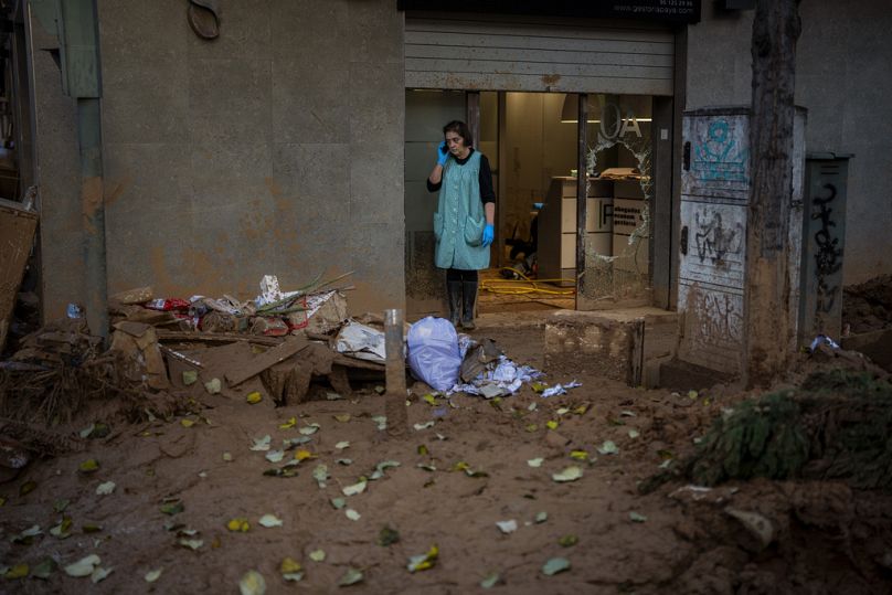 Une femme parle au téléphone depuis l'entrée d'un magasin touché par les inondations à Masanasa, Valence, Espagne.