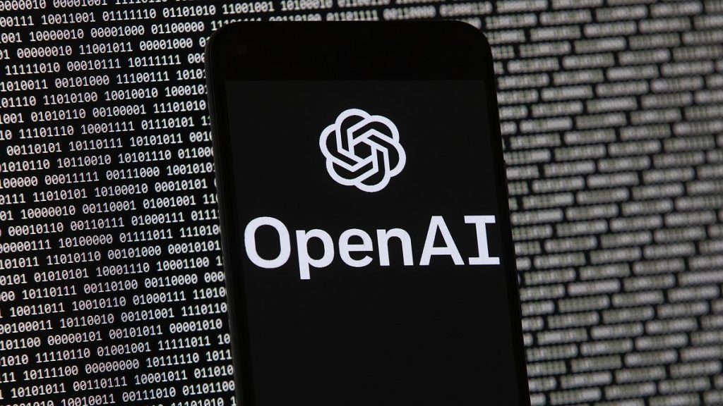 The OpenAI logo appears on a mobile phone in front of a computer screen with random binary data, March 9, 2023, in Boston.