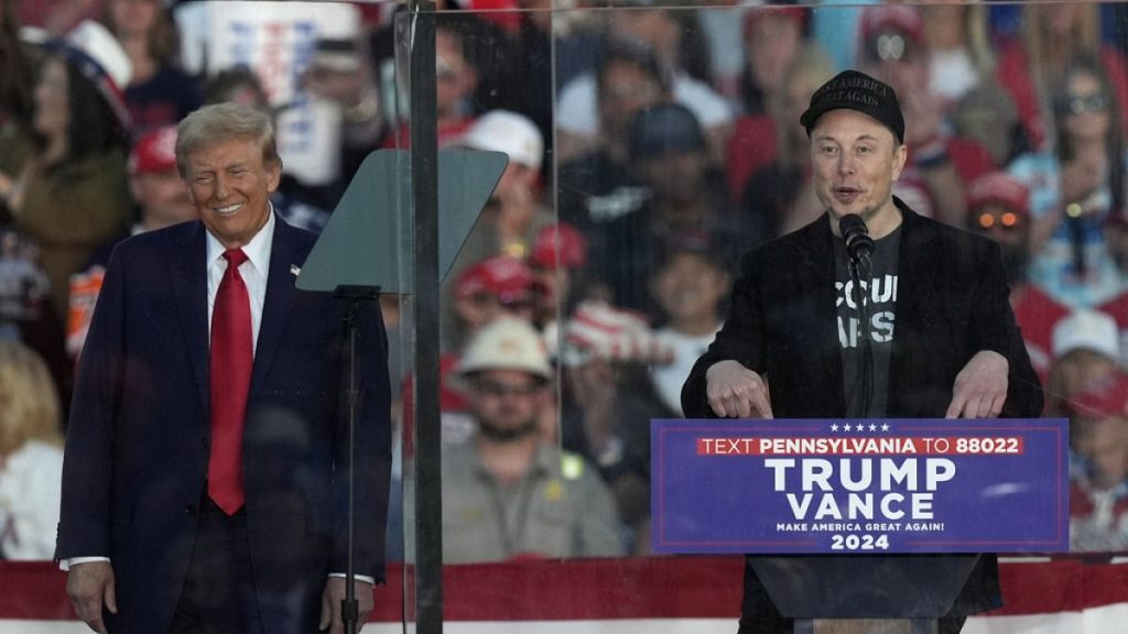 Republican presidential nominee former President Donald Trump listens as Elon Musk speaks during a campaign rally at the Butler Farm Show, Saturday, Oct. 5, 2024, in Butler, P