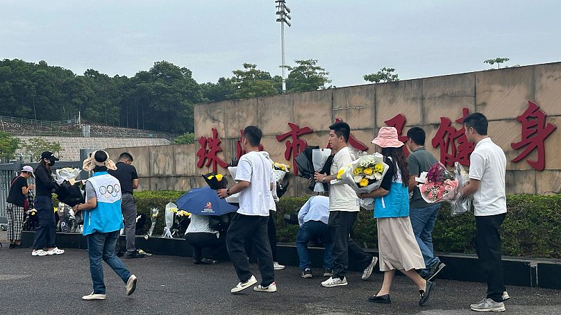 Les bénévoles déplacent les fleurs déposées à l'extérieur du "Place de remise en forme populaire de Zhuhai" le mercredi 13 novembre 2024.