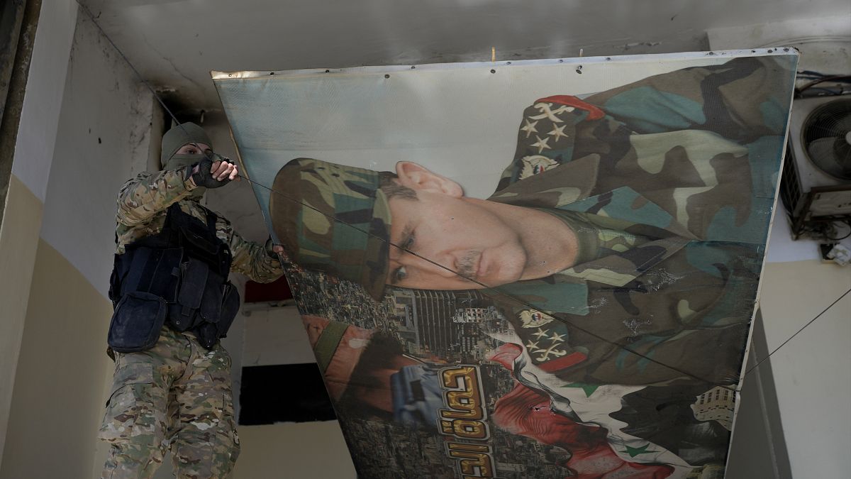 A Syrian rebel removes a poster of former President Bashar al-Assad in Damascus, 14 December, 2024