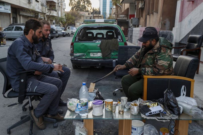 Des combattants syriens sont assis dans une rue alors qu'ils gardent un poste de police à Damas, en Syrie, le mardi 17 décembre 2024.