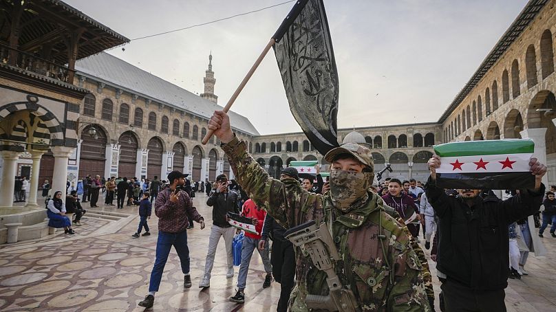 Un combattant de l'opposition masqué porte un drapeau de Hayat Tahrir al-Sham (HTS) dans la cour de la mosquée des Omeyyades de la ville de Damas, en Syrie, le mardi 10 décembre 2024.