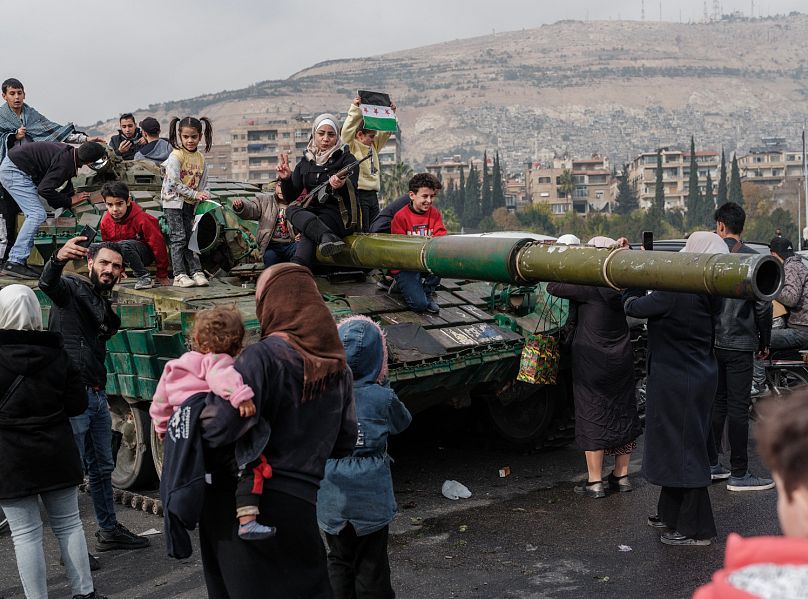 Des citoyens syriens font la fête au sommet d'un char gouvernemental abandonné à Damas, en Syrie