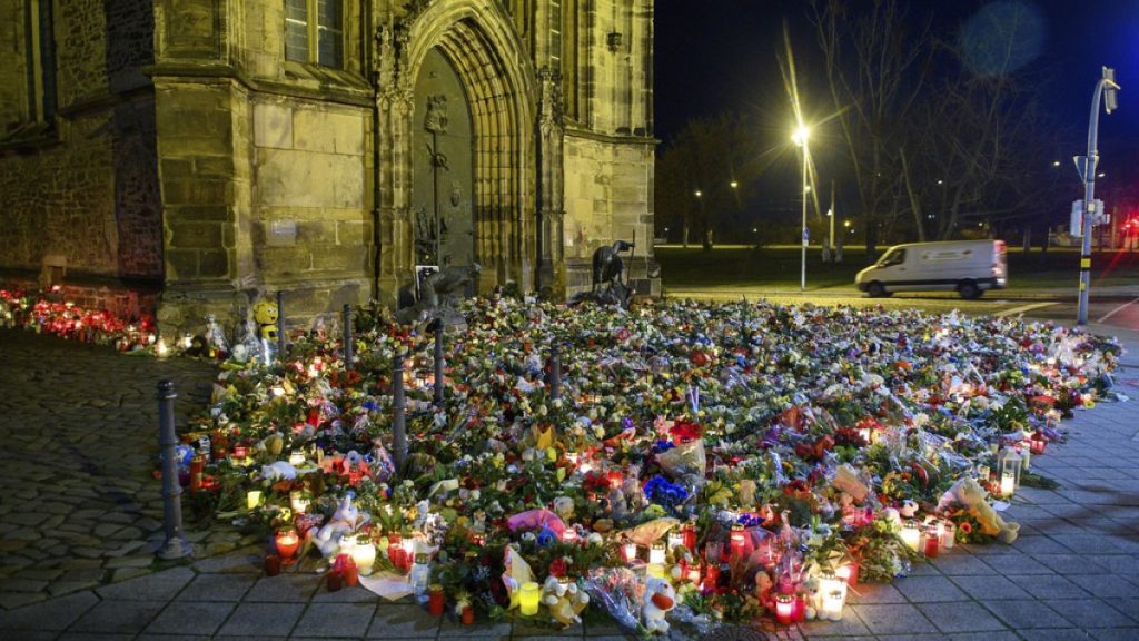 Flowers, candles, wreaths and stuffed animals lie in front of St. John