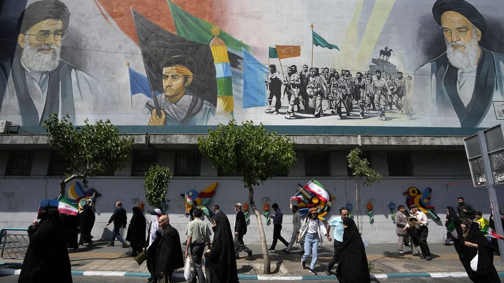 Iranian worshippers walk past a mural showing the Ayatollah Ali Khamenei, left, after Friday prayers in Tehran, 19 April, 2024