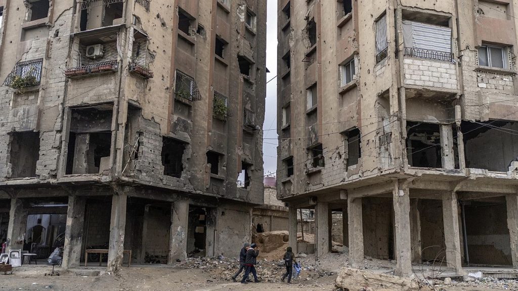 People walk between buildings that were damaged by air strikes during the al-Assad rule in Douma, 29 December, 2024