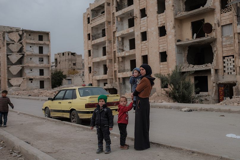 Une mère et ses enfants se tiennent dans une rue d’Alep, en Syrie, sur fond de bâtiments détruits par la guerre