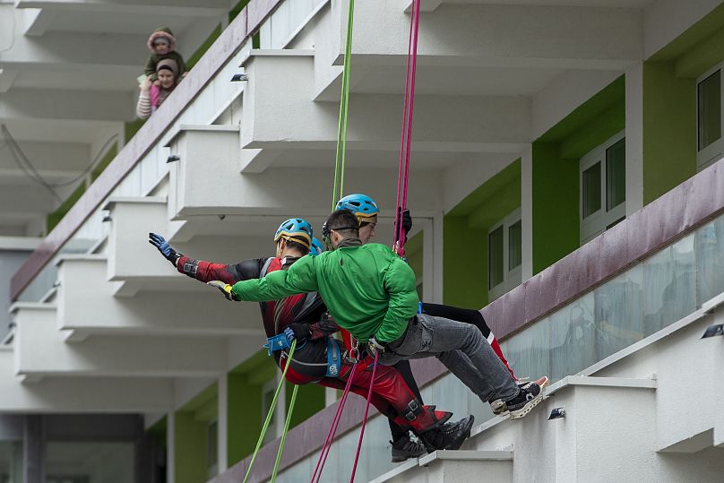 Des alpinistes du Kosovo déguisés en super-héros saluent les enfants alors qu'ils descendent avec des cordes du toit de l'hôpital pour offrir des cadeaux aux enfants à Pristina, le 13 décembre 2024.