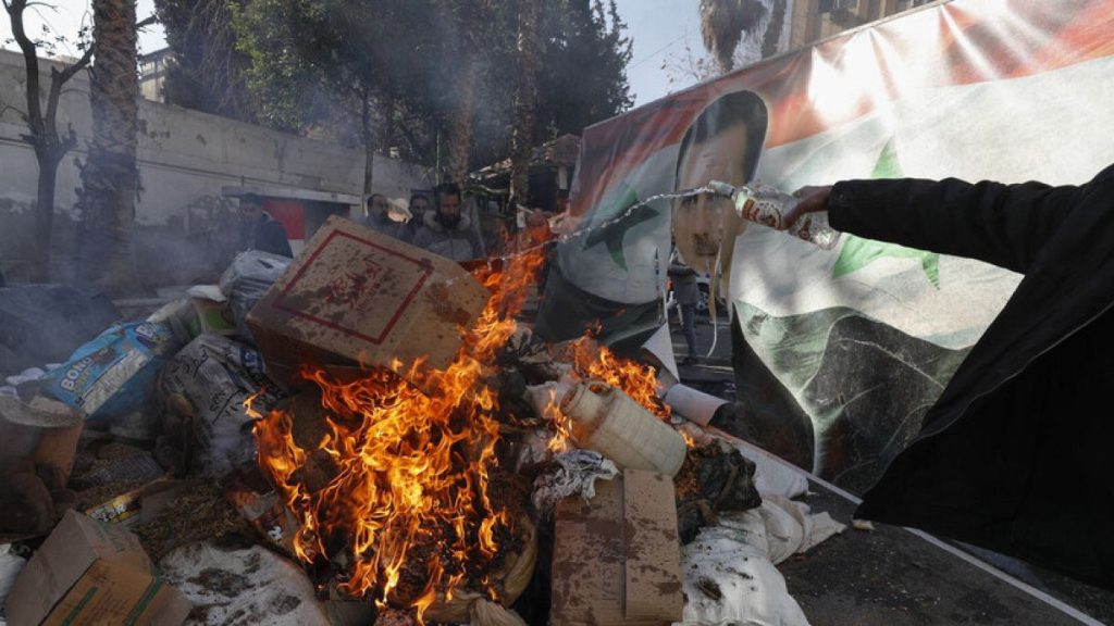 A banner of ousted Bashar al-Assad is placed on a fire as rebel forces destroys drugs and alcohol, found at a complex building, in Damascus, Syria, Wednesday, Dec. 25, 2024