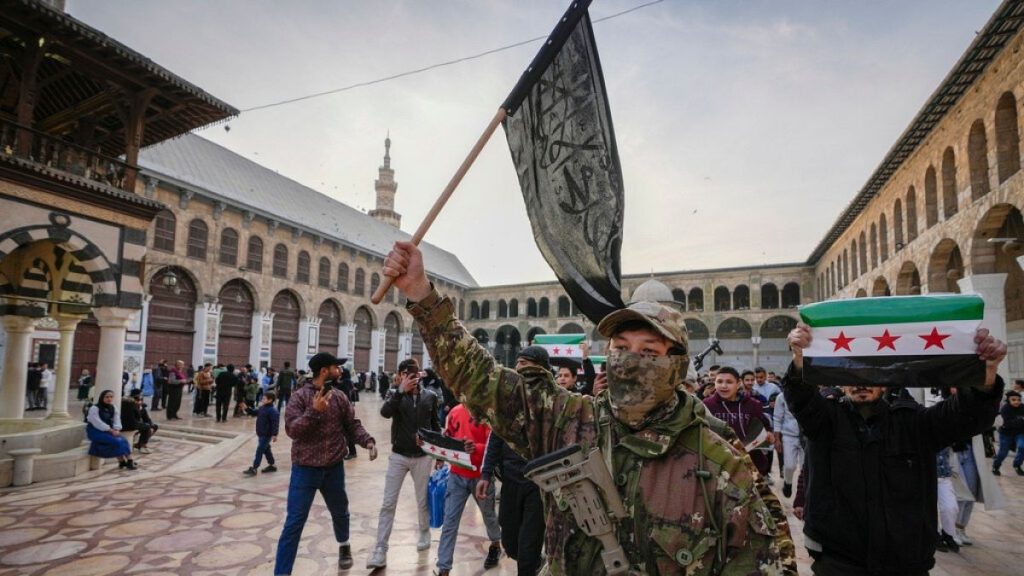 A masked opposition fighter carries a flag of Hayat Tahrir al-Sham (HTS) in the courtyard of the Umayyad Mosque in the old walled city of Damascus, Syria, 2024.