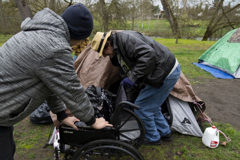 DOSSIER – Un bénévole s'accroche à un fauteuil roulant pendant qu'il aide Max Hartfelt à entrer dans sa tente après l'avoir déplacé d'un parc à un autre le 23 mars 2024, à Grants Pass, Oregon