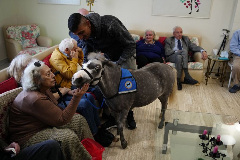 Ali Hussein, ouvrier pakistanais de 34 ans, tient dans ses bras Calypso, un cheval miniature utilisé pour des programmes thérapeutiques, lors d'une visite dans une maison de retraite à Athènes, en Grèce, vendredi.