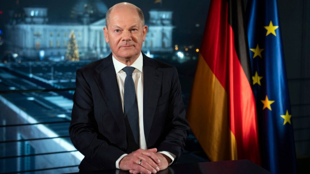 German Chancellor Olaf Scholz sits in front of the backdrop of the Reichstag illuminated by spotlights during a photo session after the recording of his New Year