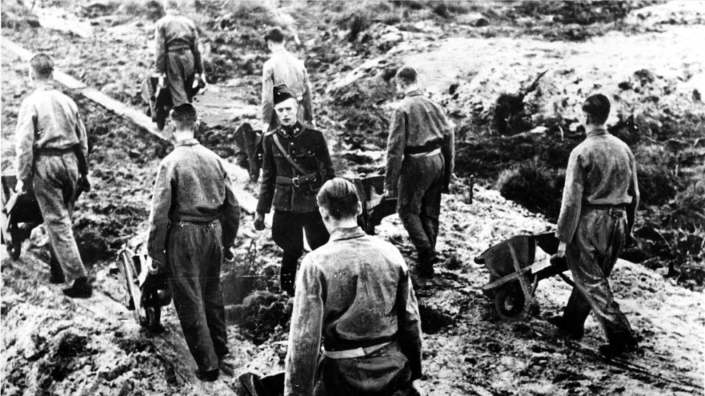 Prisoners of the Dutch Labour Corps work in chain gang fashion under a Nazi foreman in a forced labour camp in the Netherlands, 2 March, 1944