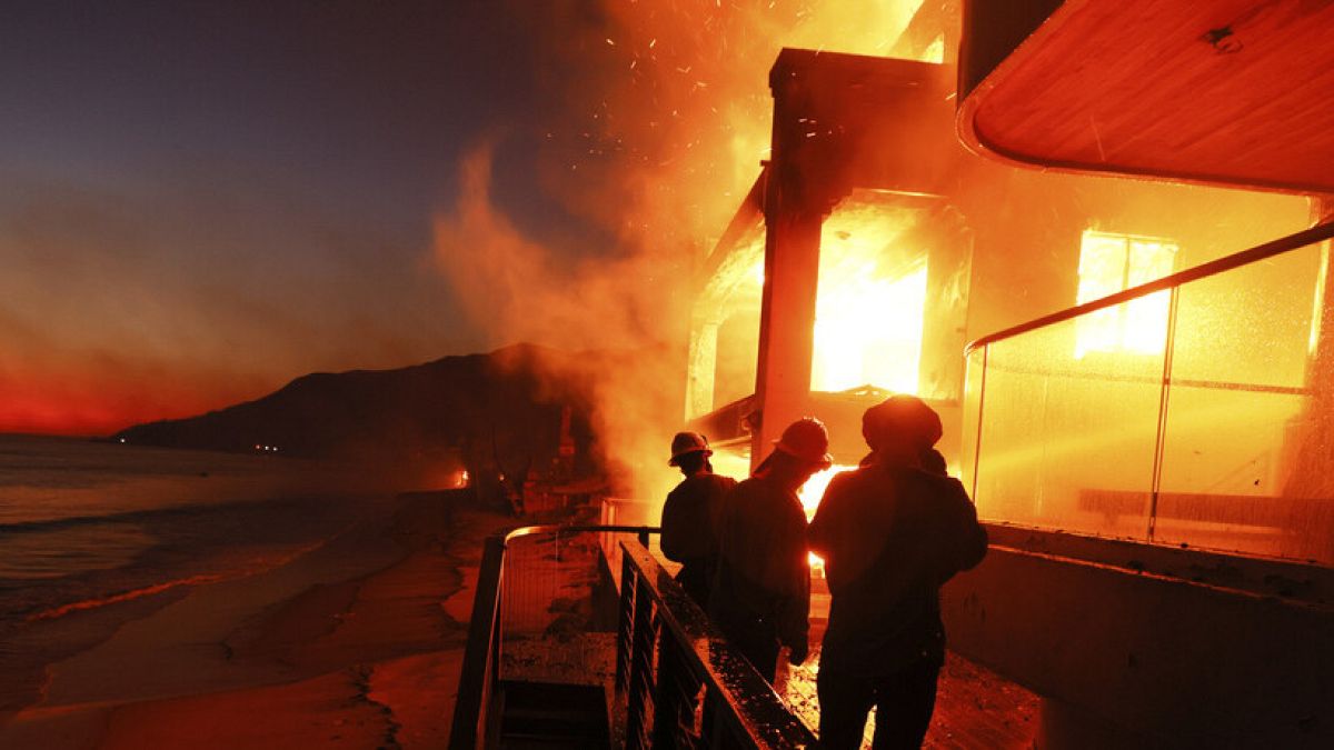 Firefighters work from a deck as the Palisades Fire burns a beach front property Wednesday, Jan. 8, 2025 in Malibu, California