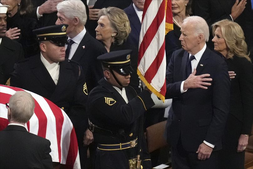 Le président Joe Biden et la première dame Jill Biden regardent une équipe de porteurs de corps des services communs porter le cercueil de l'ancien président Jimmy Carter lors des funérailles d'État.