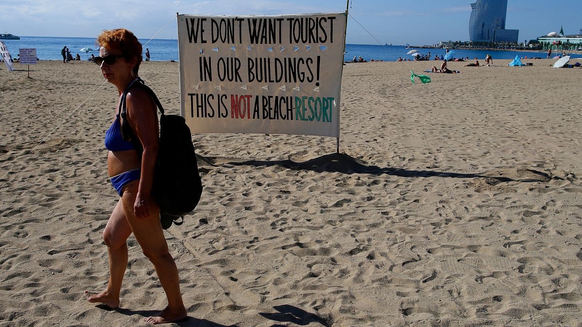 A woman walks past a banner during a protest against tourism in Barcelona, Spain.