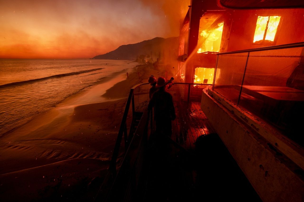 Les pompiers travaillent depuis une terrasse alors que l'incendie des Palisades brûle une propriété en bord de mer, le 8 janvier 2025, à Malibu, en Californie. 