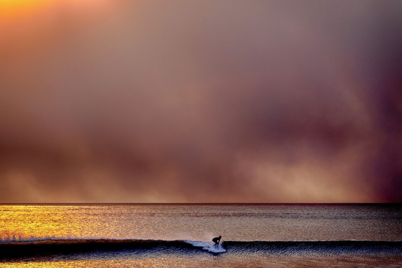 Un surfeur décolle sur une vague à Santa Monica, en Californie, au coucher du soleil sous un ciel noirci par l'incendie des Palisades dans les Pacific Palisades, le 7 janvier 2025.