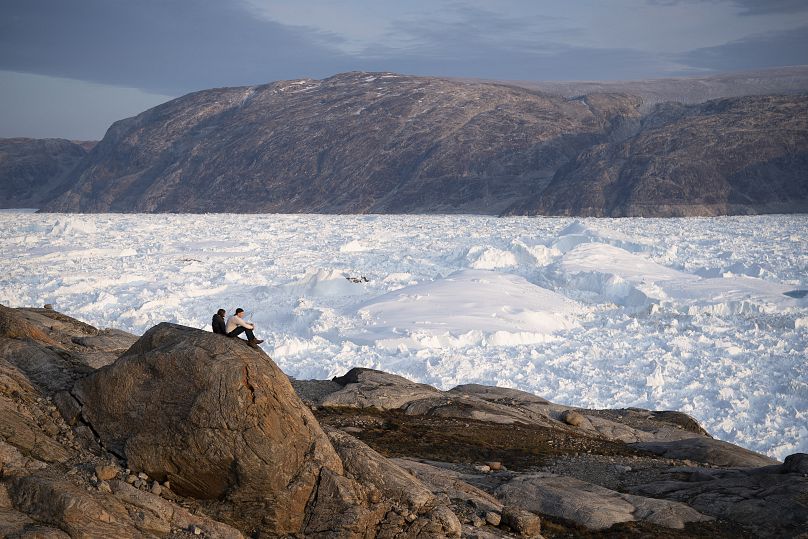 Des étudiants chercheurs de l'Université de New York sont assis sur un rocher surplombant le glacier Helheim au Groenland, le 16 août 2019. 