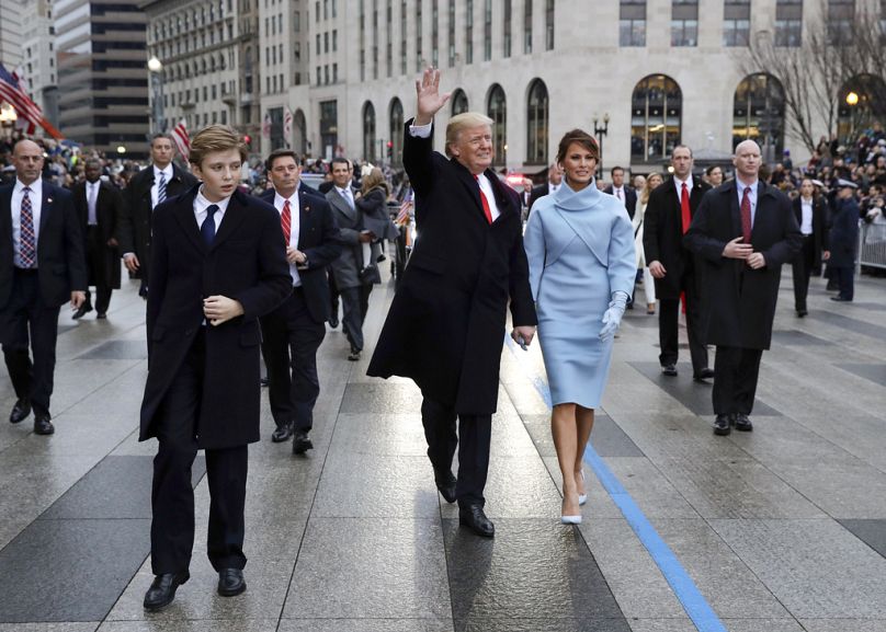 DOSSIER – Le président Donald Trump salue alors qu'il marche avec la première dame Melania Trump et leur fils Barron, lors du défilé d'inauguration sur Pennsylvania Avenue à Washington.