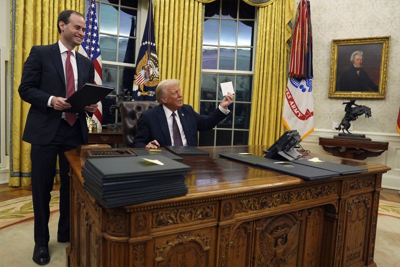 Le président Donald Trump brandit une lettre de l'ancien président Joe Biden alors qu'il signe des décrets dans le bureau ovale de la Maison Blanche, le lundi 20 janvier 2025.