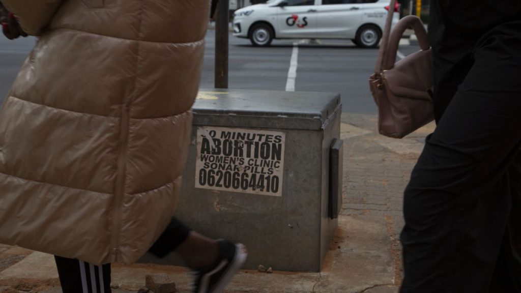 Women pass a sticker advertising abortion pills in Johannesburg, South Africa, in June 2023.