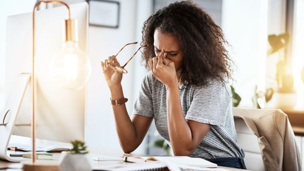 A woman rubs her eyes after working at a computer.