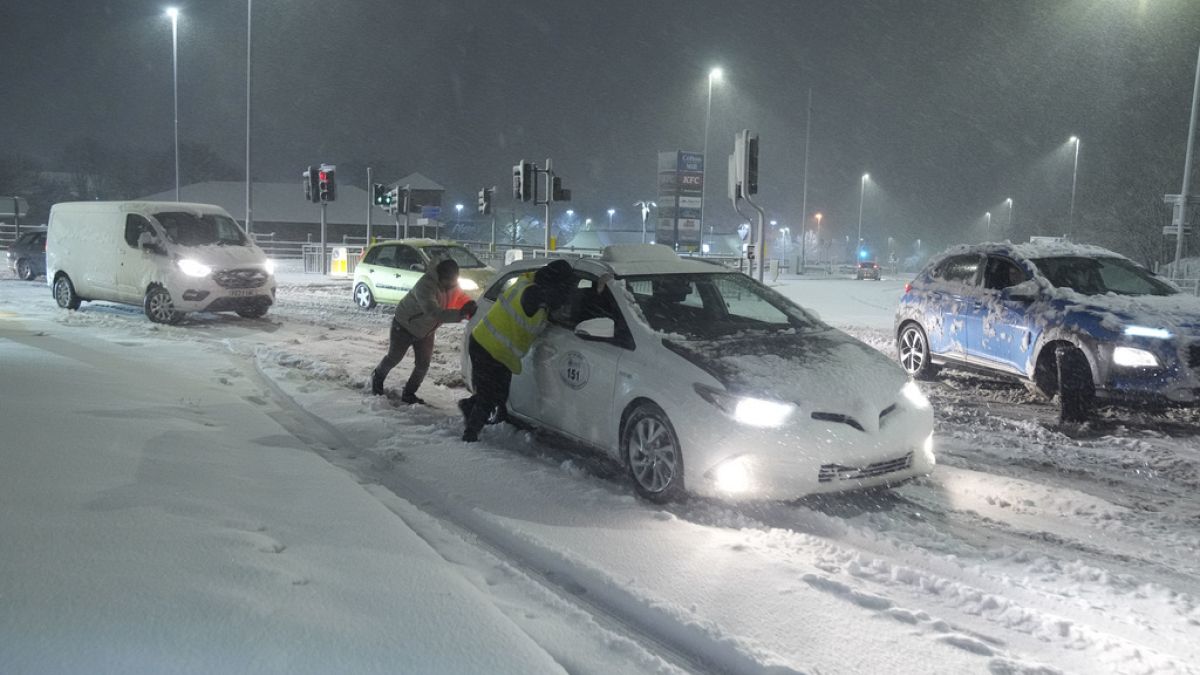 People help to push cars stuck in snow in Leeds, England, Sunday, Jan. 5, 2025.