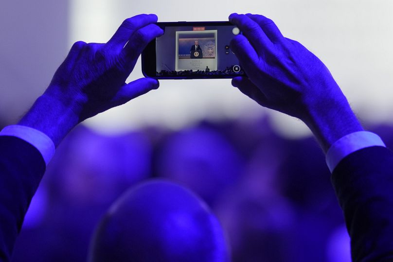   Un homme prend des photos lors d'un discours virtuel du président américain Donald Trump lors de la réunion annuelle du Forum économique mondial à Davos, janvier 2025.