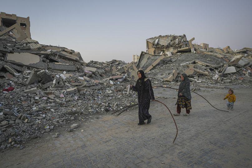 Deux femmes palestiniennes transportent des barres de métal récupérées dans les ruines pour renforcer leurs tentes dans leur camp de la ville de Khan Younis, le 1er janvier 2025.