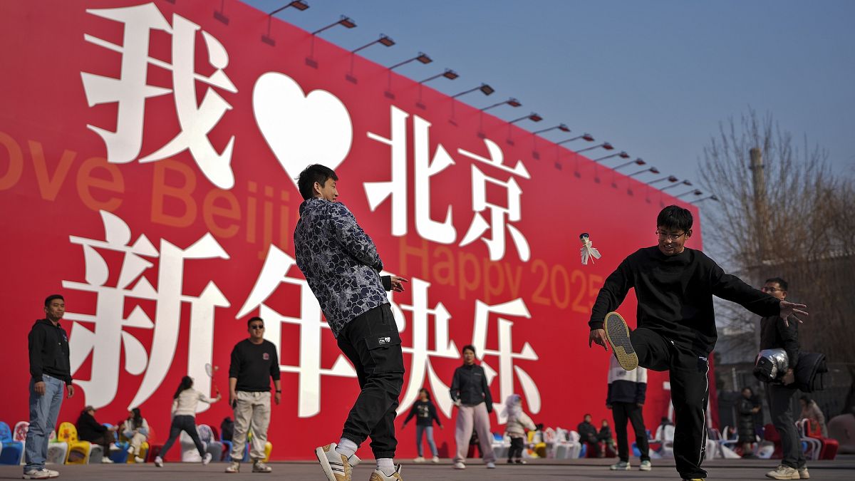 Chinese people play shutter cock near a huge display board with the words,