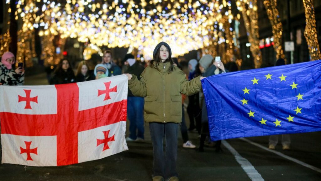 Demonstrators hold a Georgian national and an EU flag as they listen to outgoing Georgian President Salome Zourabichvili during an anti-government rally outside parliament