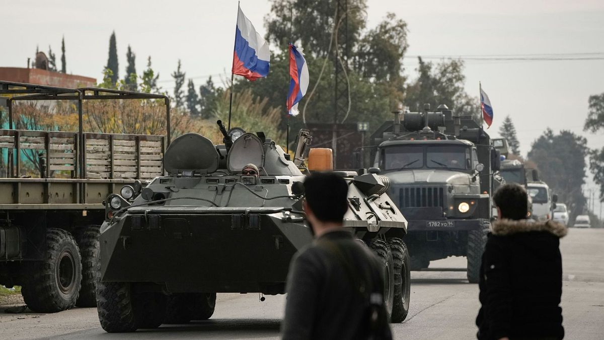 FILE - Syrian fighters watch Russian armoured vehicles driving past near the Hmeimim Air Base, a Syrian airbase currently operated by Russia, 16 December 2024.