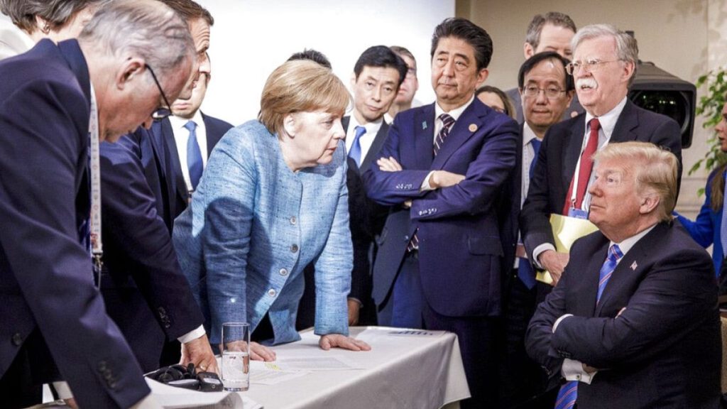 FILE - Former German Chancellor Angela Merkel, speaks with U.S. President Donald Trump, seated at right, at G7 Summit in La Malbaie, Quebec, Canada, June 9, 2018.