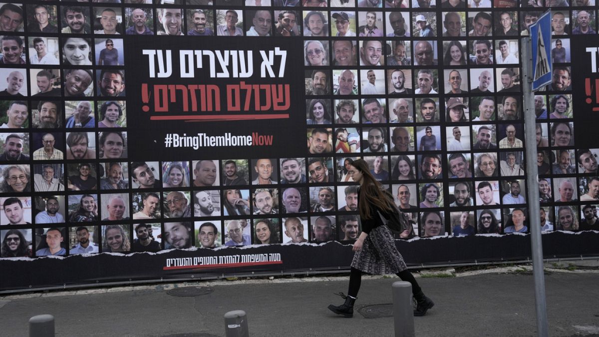 FILE - A woman walks past photos of hostages held by Hamas in the Gaza Strip, in Jerusalem, Friday, Jan. 17, 2025. (AP Photo/Mahmoud Illean)