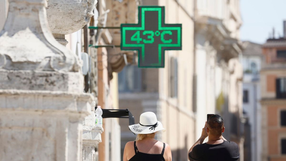 A man takes a photo of the temperature of 43C recorded in the sun outside a pharmacy in downtown Rome.