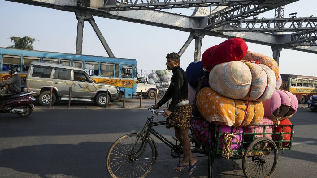 A man on a transport rickshaw with sacks of garments crosses the Howrah Bridge over Hooghly River in Kolkata, India. 28 December 2024.