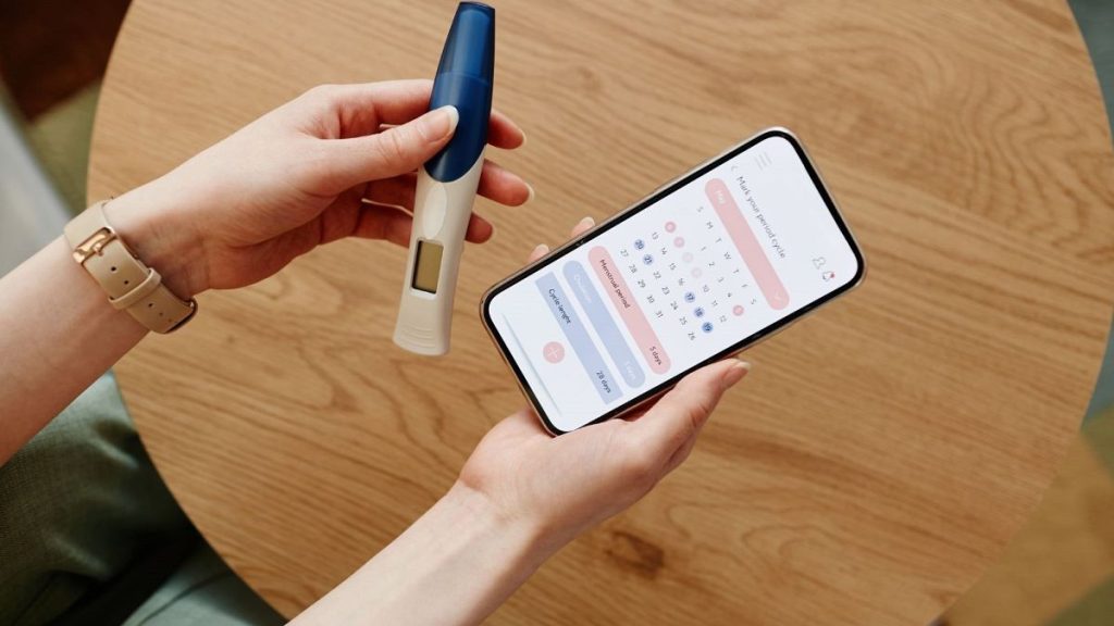 A woman uses an app to calculate her menstrual cycle while holding a pregnancy test.