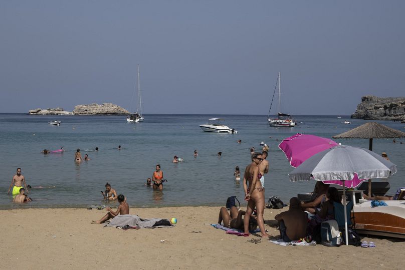 Les touristes profitent de la plage et de la mer à Lindos, sur l’île de Rhodes, dans la mer Égée, dans le sud-est de la Grèce.