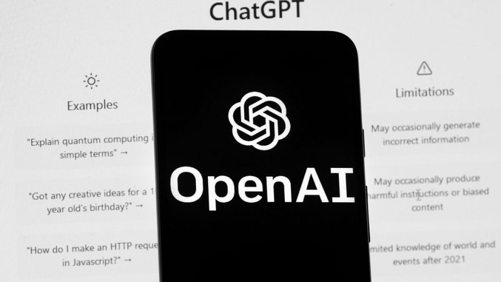 The OpenAI logo is seen on a mobile phone in front of a computer screen which displays the ChatGPT home Screen, on March 17, 2023, in Boston